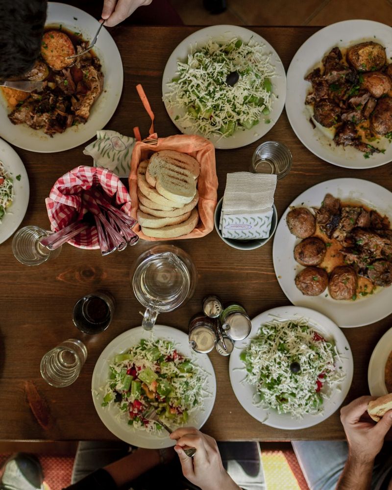 Sharing plates of salads and roast meats laid across a wooden table, seen from above