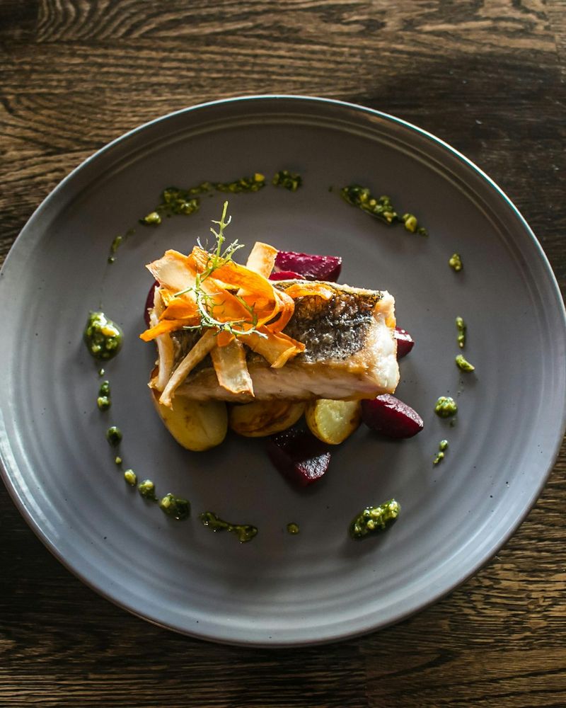A plated fish course on a grey plate, set on a dark wooden table