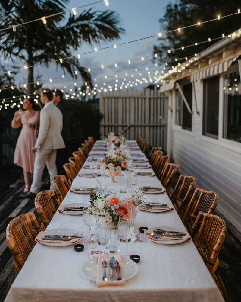 A long outdoor wedding table under festoon lights