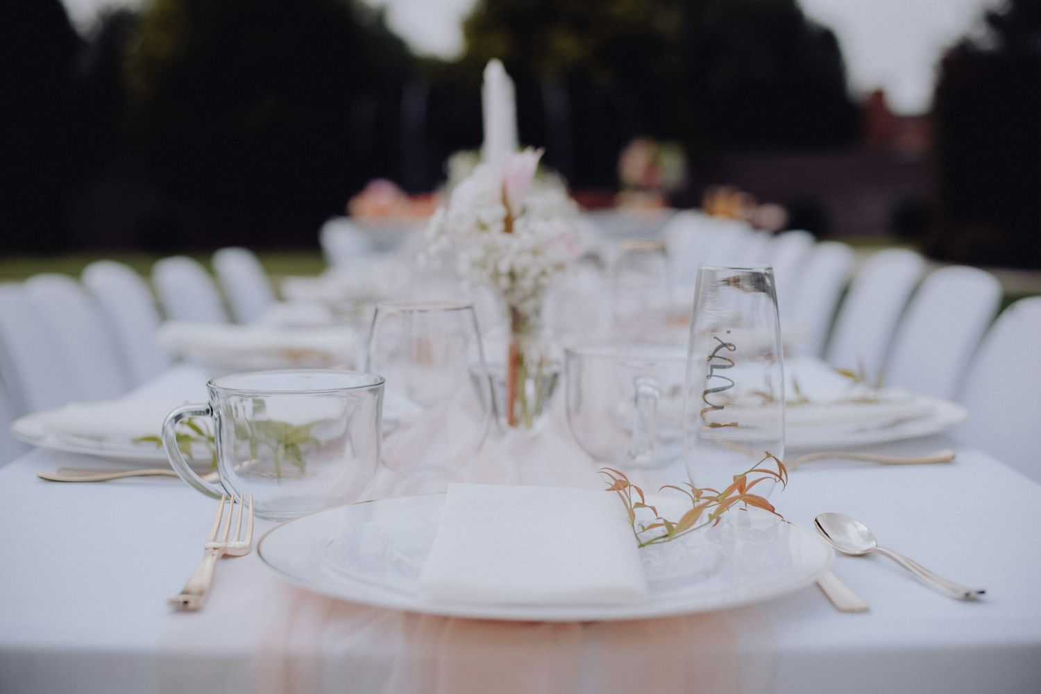 A wedding table set outdoors with white linen, glassware and flowers