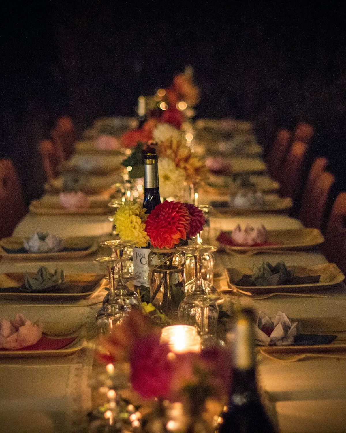 A long dinner table lit by candles, set with flowers and plates